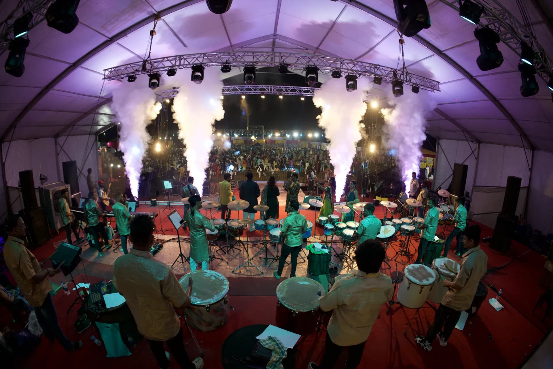 Dhol players performing on stage as smoke fountains rise behind them